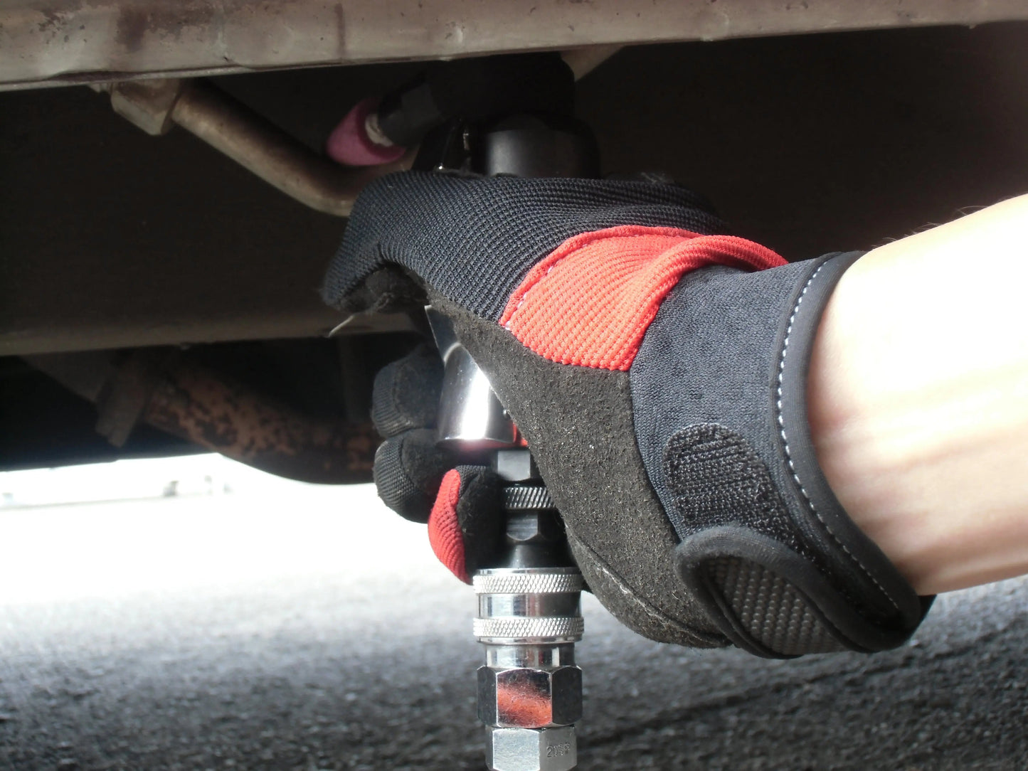 a person wearing gloves and holding a wrench under a vehicle